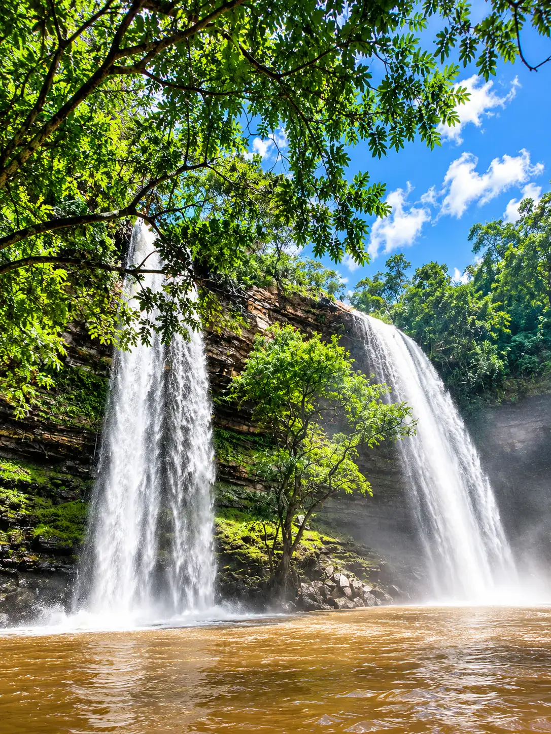 Twin waterfalls falling into a pool in a lush green gorge