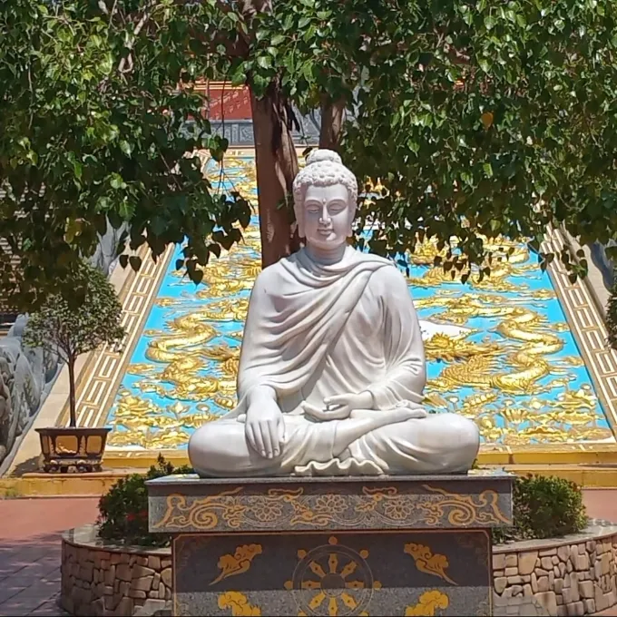 White seated Buddha statue in front of an ornate golden mural